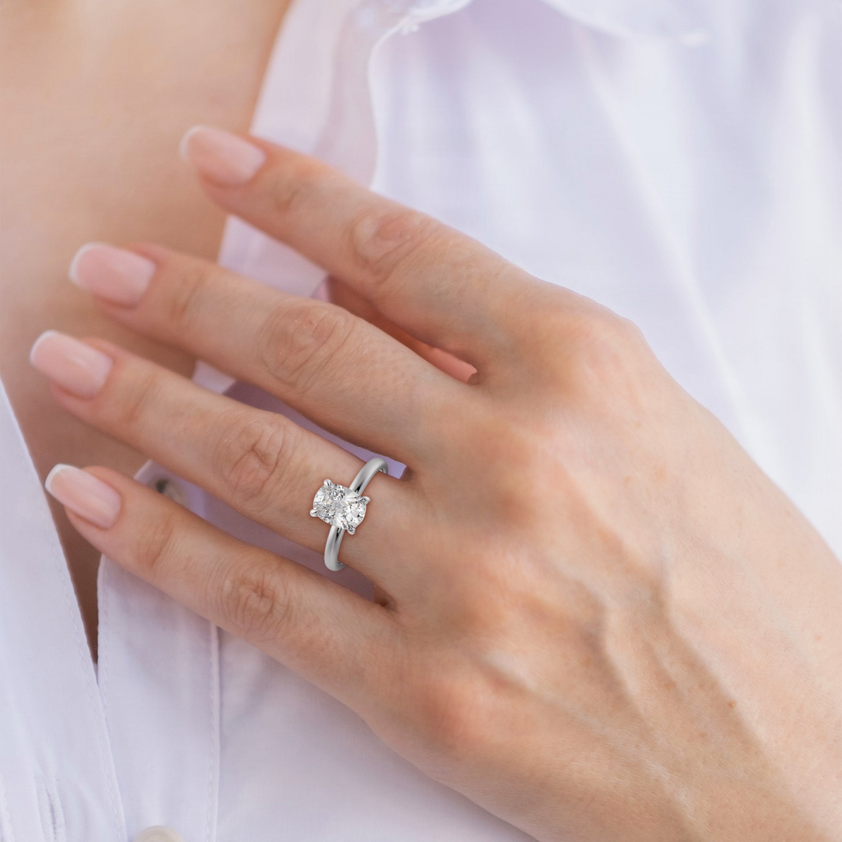 Diamond cushion solitaire ring on hand, slender band with four-prong setting